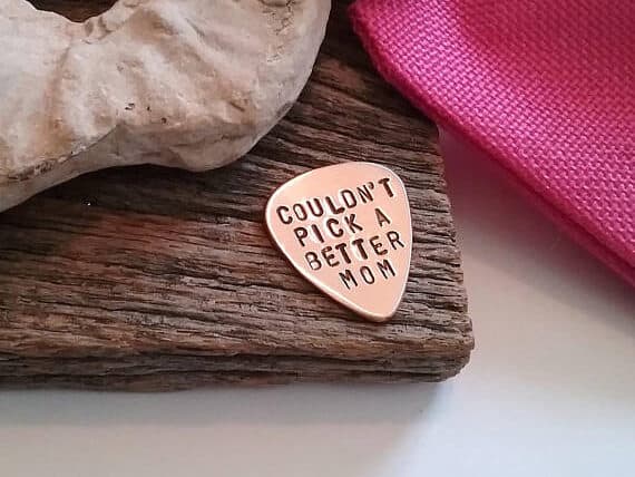 Rose gold guitar pick engraved with black font that reads couldn't pick a better mom. 
