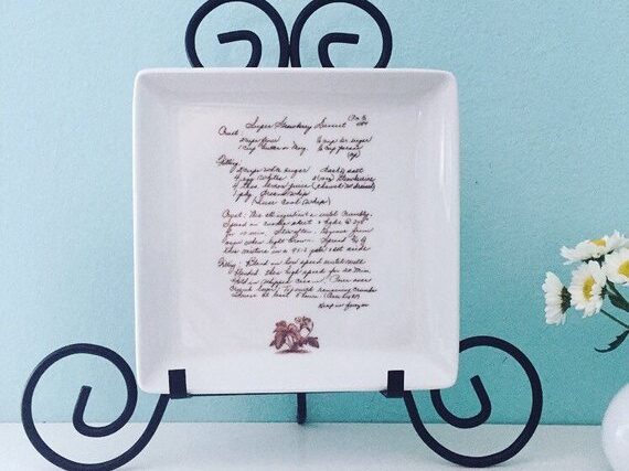 White square plate on a black plate holder with a handwritten recipe on it. 