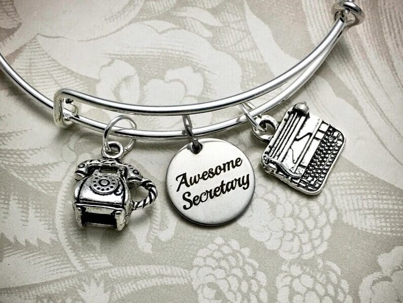 Gift Ideas for Secretary Day That Aren't Flowers: silver charm bracelet with three charms hanging from it, one a telephone, one a round circle that says awesome secretary and one a type writer.
