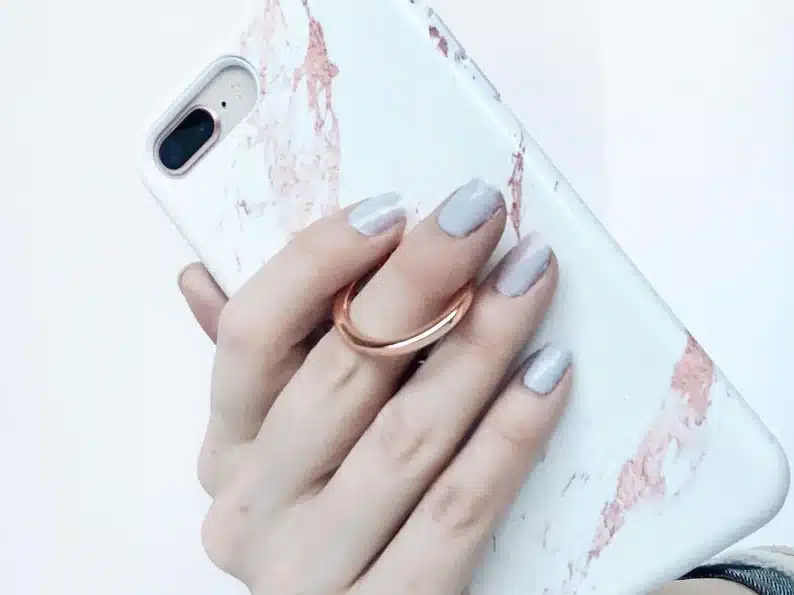 Hand holding a white and rose gold marble phone case with a rose gold ring to help hold the case. 