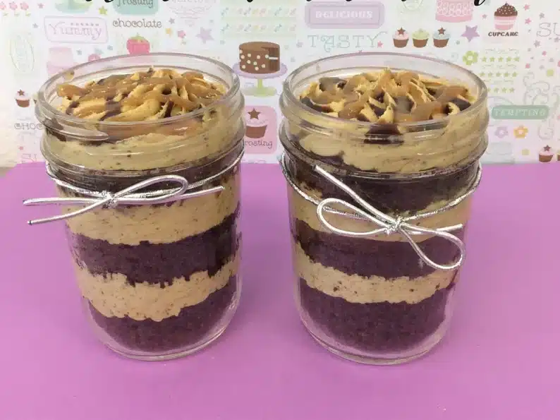 Two cupcakes in a jar, two clear jars with layered chocolate and icing cupcakes each with a thin silver bow on it. 