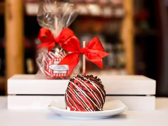 Apple dipped in cherry chocolate chip with caramel sauce with a red bow on the end of the white stick. 
