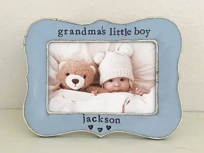 Blue frame with black font that says Grandma's little boy at the top and at the bottom Jackson with three black hearts. with a photo of a little boy with a knitted white hat on with a brown teddy bear beside him. 