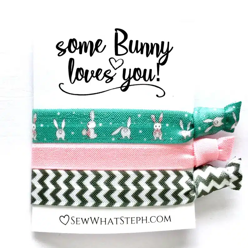 Three hair ties: green with white bunnies on it, solid pink, and black and white zig zag on a white paper that says Some bunny loves you! 