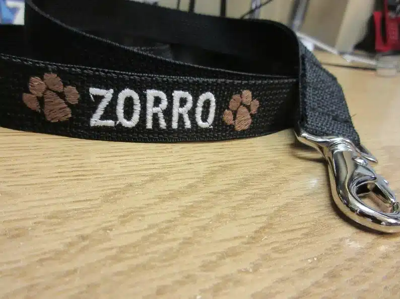 Black dog leash with white stitched on font that says ZORRO with two brown paw prints on each side 