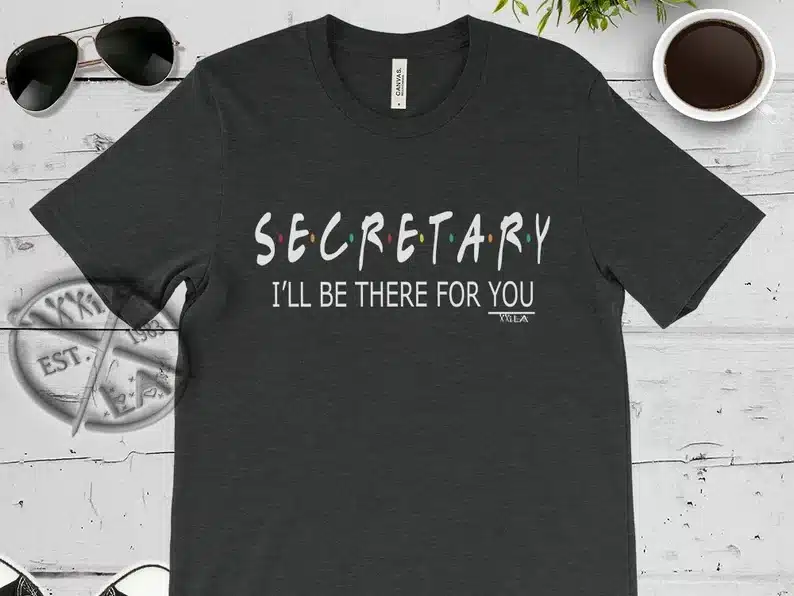 Black t-shirt with white font that says "S-E-C-R-E-T-A-R-Y I'll be there fo ryou" in the style of the show friends. 