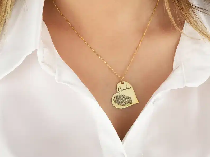 Gold necklace with a heart pendant with the name and a thumb print on it. 