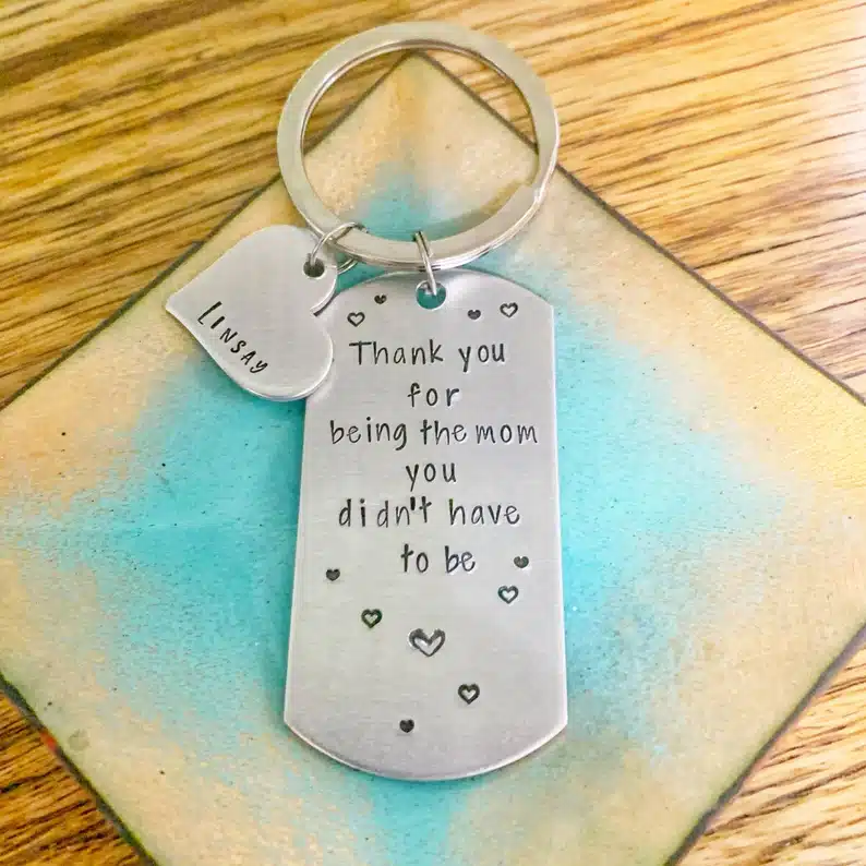 Dog tag charm on a key chain with another charm that's a silver heart both engraved with black font. 