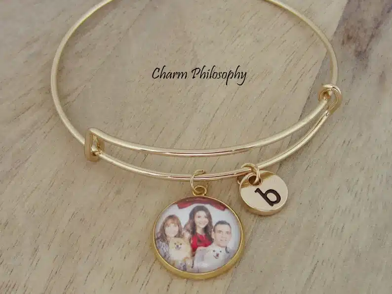 Mother's Day Gift for Your Ex Wife: Gold charm bracelet with a small framed round photo charm of a family with dogs and a smaller round charm with a lower case b on it. 