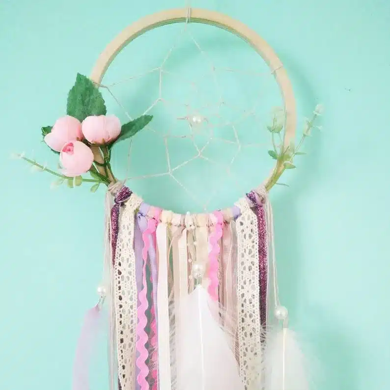 Blue background with a dreamcatcher shown with various pinks, purples, and white hanging ribbon. 