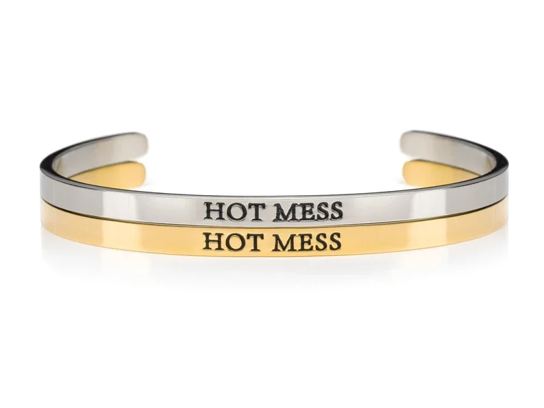 Two cuff bracelets, one silver and one gold. Both with black font that says HOT MESS on them. 