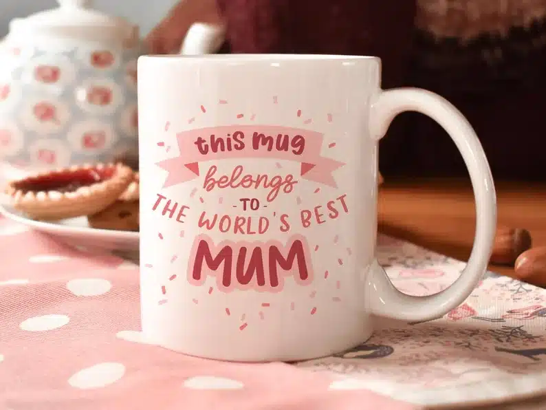 White coffee mug with pink font that says this mug belongs to the world's best mum with pink confetti around font. 