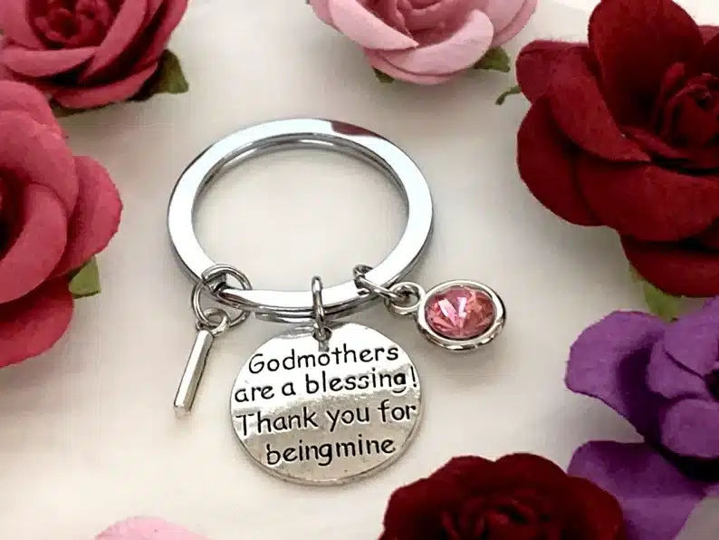 Silver keychain with a round charm engraved in black that reads godmothers are a blessing! Thank you for being mine, with a pink charm hanging beside it. 