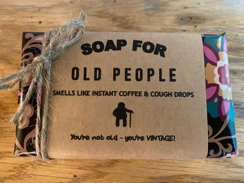 Soap wrapped in colorful wrapping paper with brown label and string that says Soap for old people smells like insatnt coffee & cough drops. 