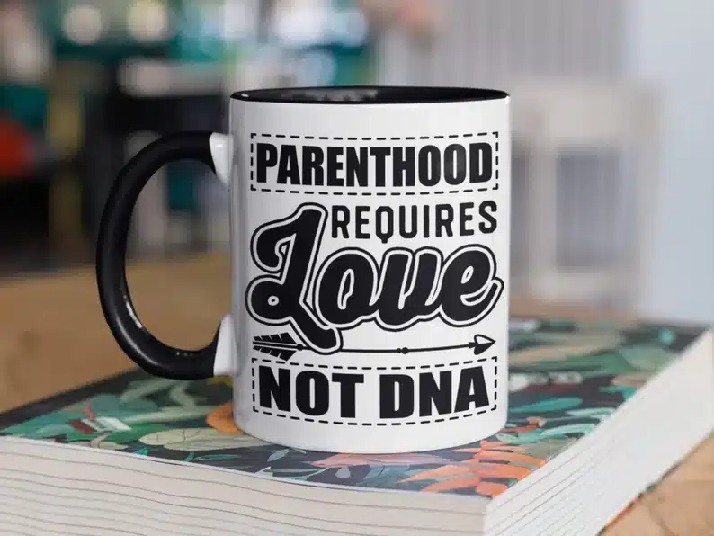 White coffee mug with black handle with black font that reads parenthood requires love not DNA 