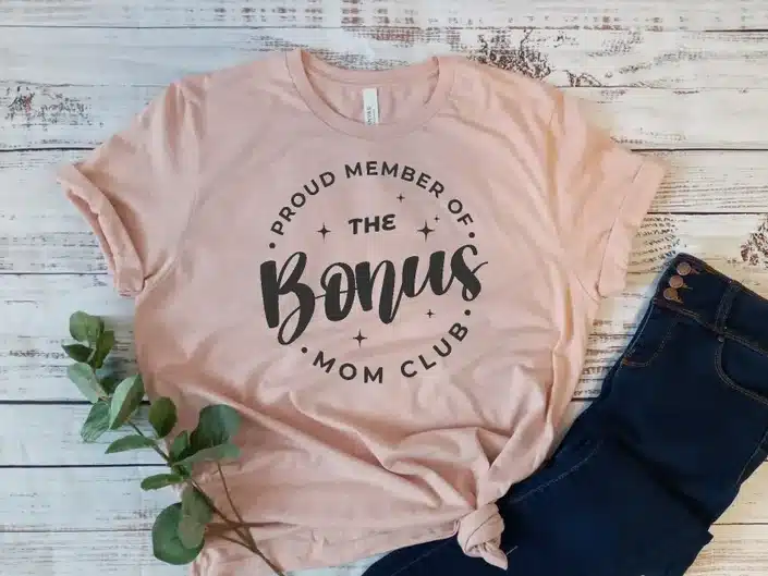 Light pink t shirt with black font that says proud member of the bonus mom club.. 