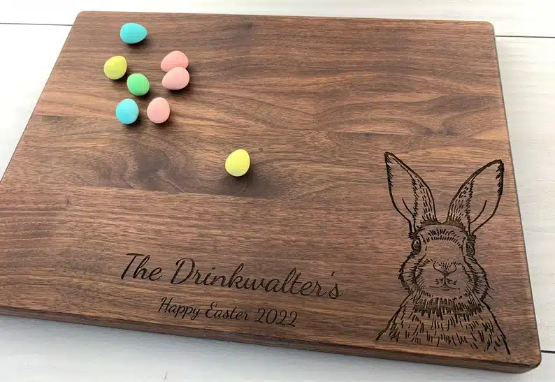 Wooden cutting board engraved with family last name, happy Easter, and a bunny. With some mini eggs on top. 