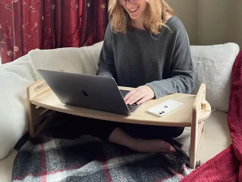 Mother's Day Gifts for Crafty Moms: showing a woman sitting on her couch with a wooden lap table with her laptop on it. 