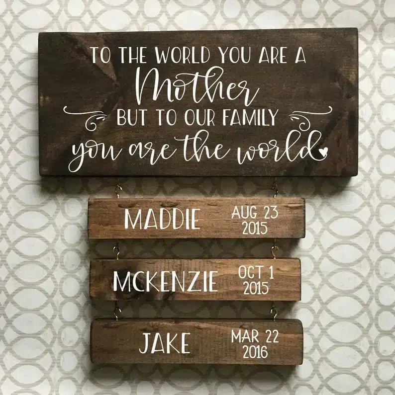Wooden large sign that says To the world you are a mother but to our family you are the world and smalled signs attched below each with a childs name and their birthdates on it. all painted in white paint. 