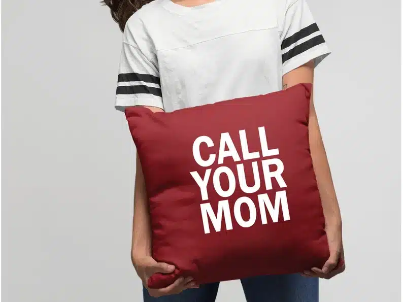 Burgundy square pillow with white font that says CALL YOUR MOM 