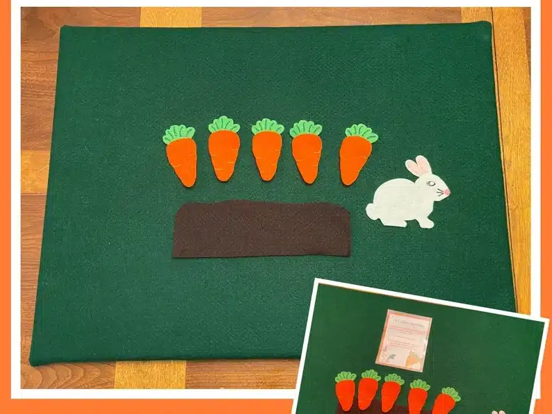 Green felt board with carrots, white bunny, and dirt on it. 