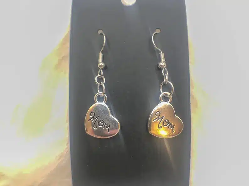 Gold earrings that are heart shaped with MOM in black font on each one. 