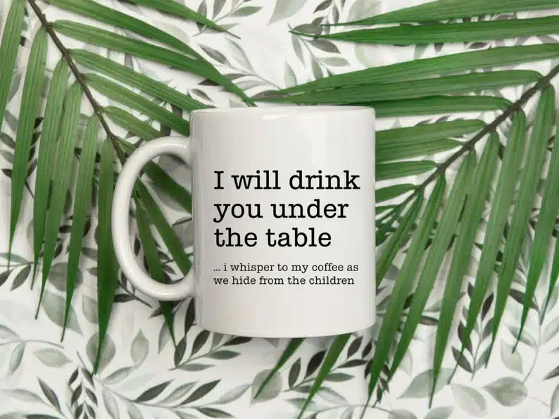 White coffee mug with black font that says I will drink you under the table...I whisper to my coffee as we hide from the children. 