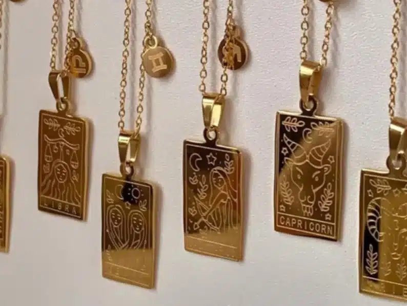 Showing many different gold necklaces with long rectangle necklace charm each with a different zodiac. 