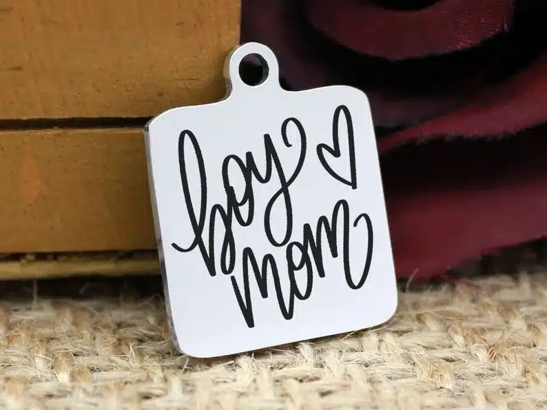 Close up of a white square charm that says BOY MOM with a heart. 