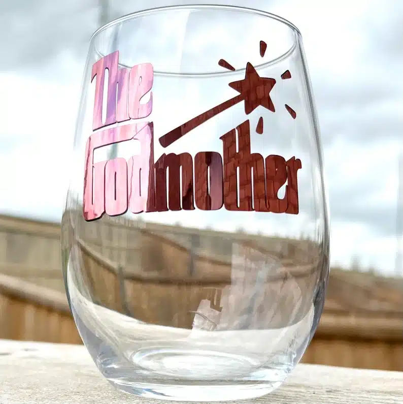 Clear stemless wine glass with the godmother in red font . 