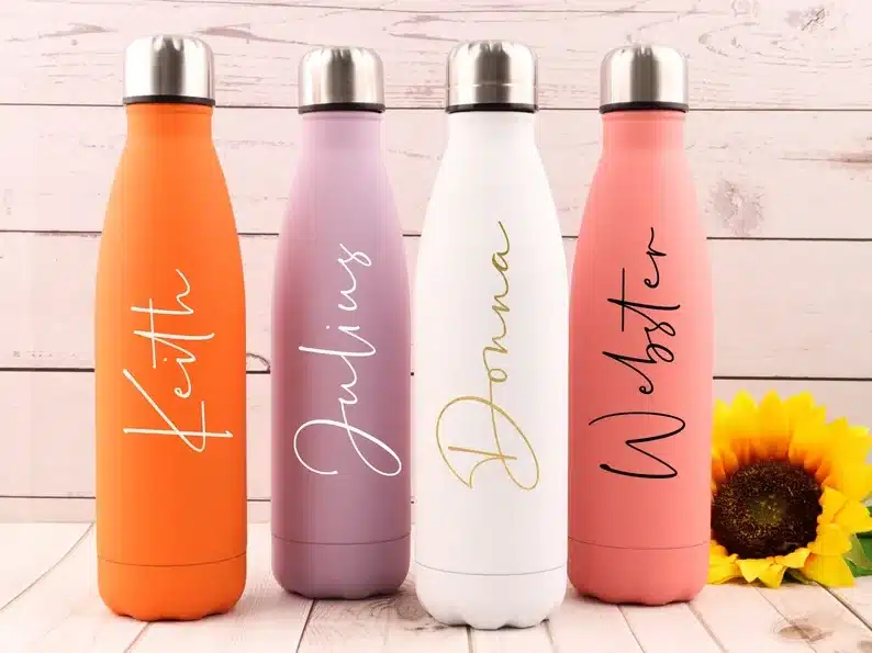 Four tall custom water bottles, orange, liliac, white, and light pink colors. all with different names on them. 