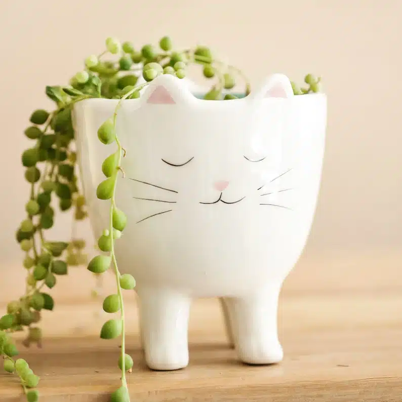 White cat planter with a green plant hanging over the side. 