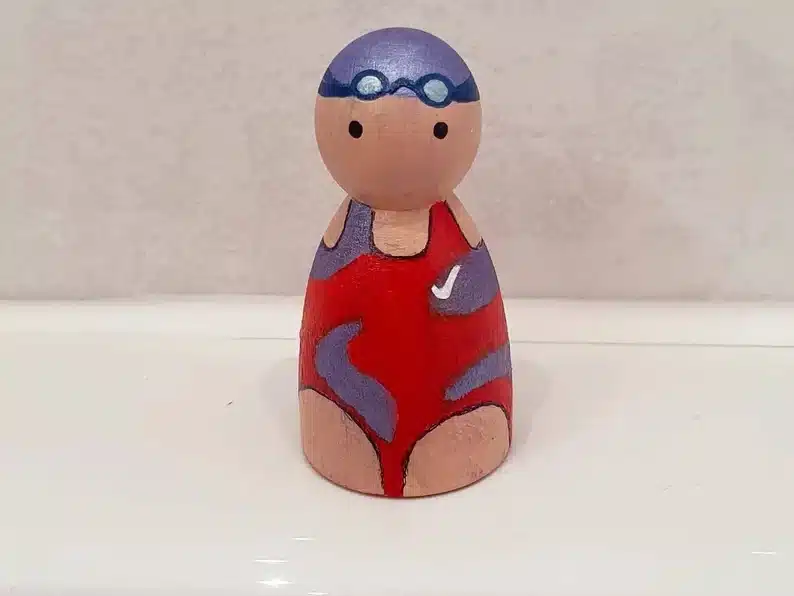 Personalized peg doll, showing a wooden person in a red bathing suit with a blue swim cap on top. 