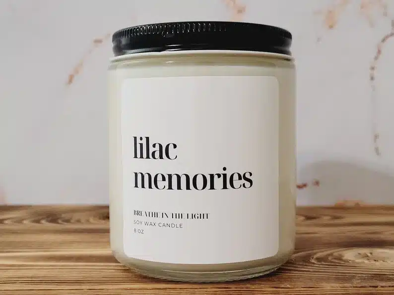 Large candle in a jar with white label with black font that says lilac memories. 