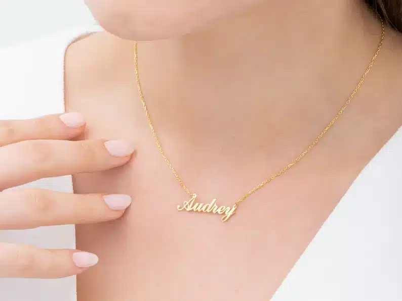 Woman wearing a gold chain necklace with the name Audrey on it. 