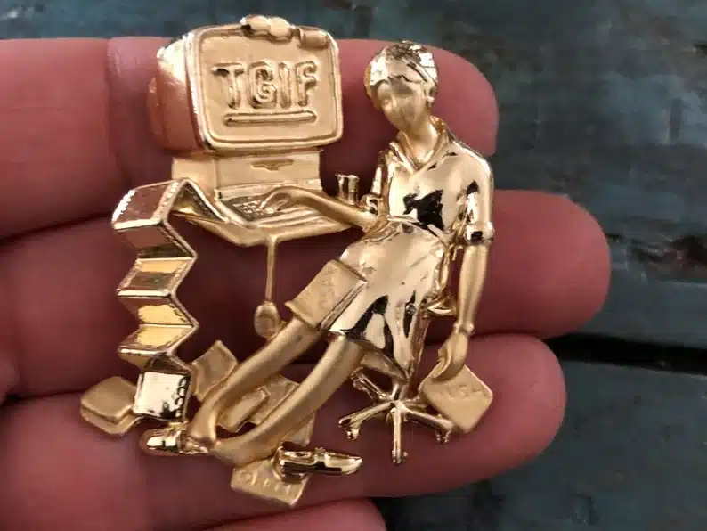 Bronze pin showing a very tired secretary on a computer that says TGIF. 