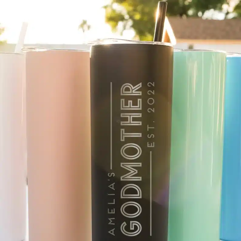 Five tall stainless steel tumblers, light pink, pink, black (engraved with silver that says Amelia's godmother est 2022), mint and blue colored tumblers. 
