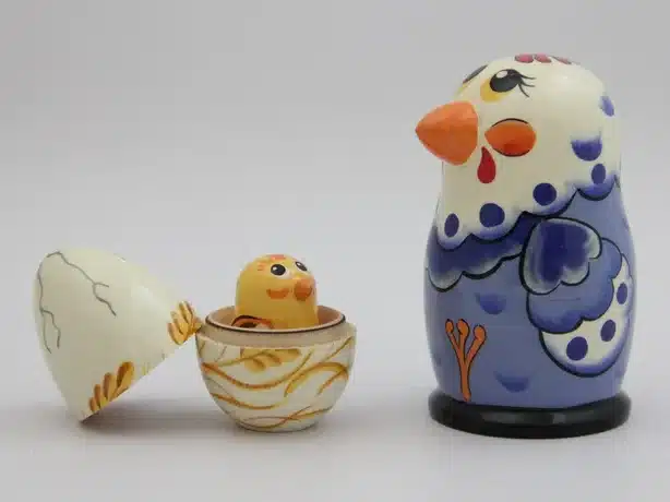 Nesting dolls, large chicken that's blue and white, with a smaller white egg opened showing a tiny yellow chick. 