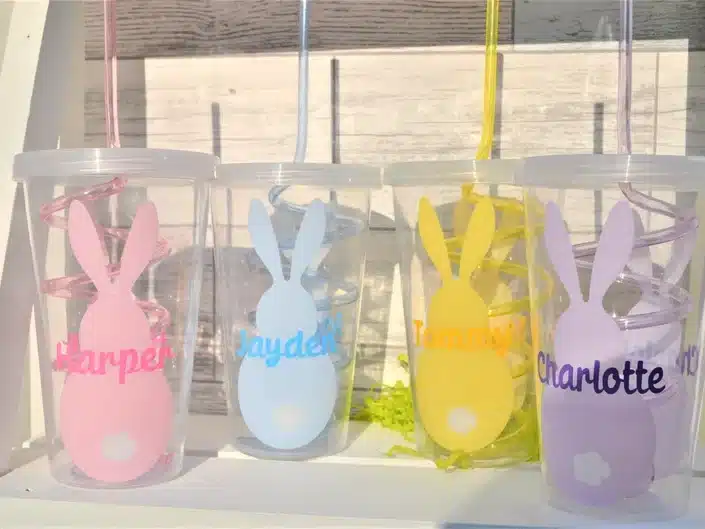 Four clear custom cups with bunnies on it and a Childs name, one pink, blue, yellow, and purple. 