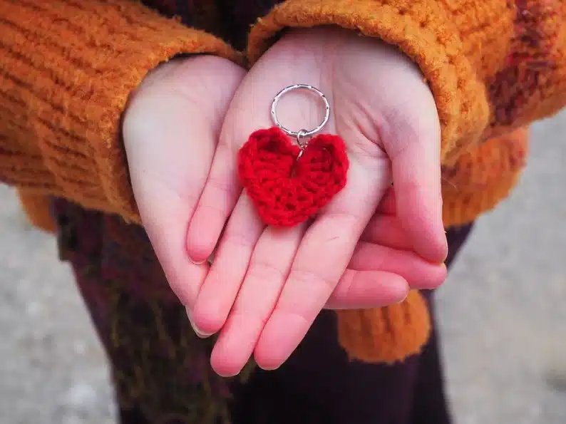 Hands holding a knitted heart keychain. 