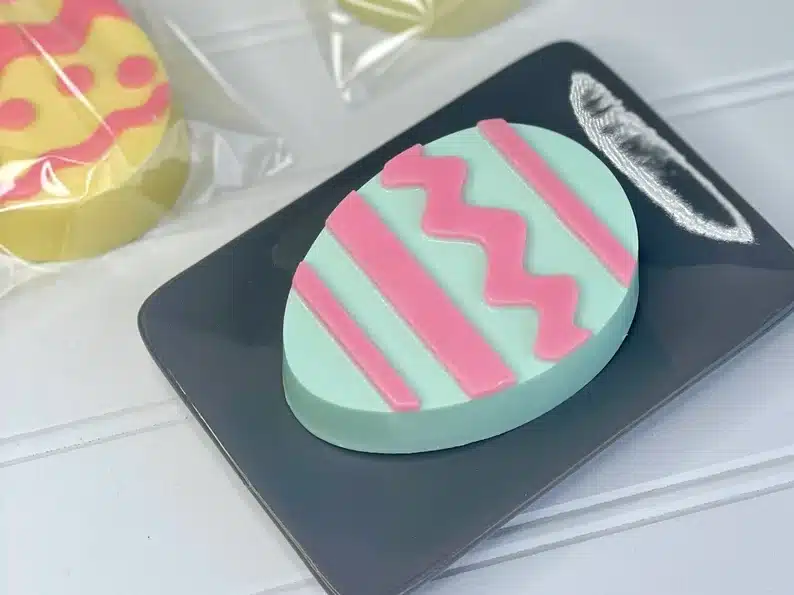 Dark grey soap dish with a teal and pink striped Easter egg made of soap. 