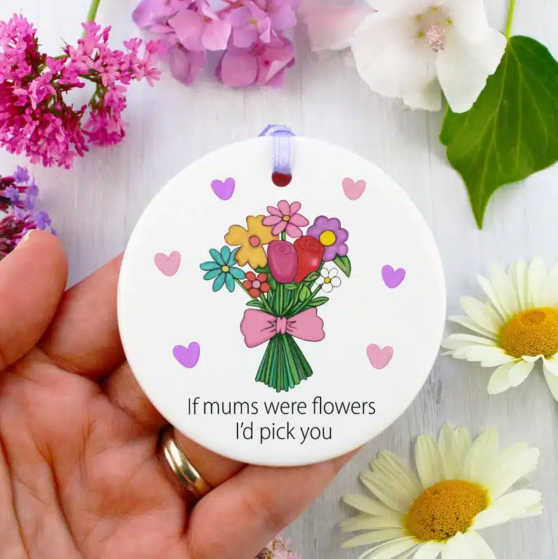 Hand holding a round white circle ornament with pink and purple hearts around a bouquet of flowers and under it in black font it says If mums were flowers i'd pick you. 