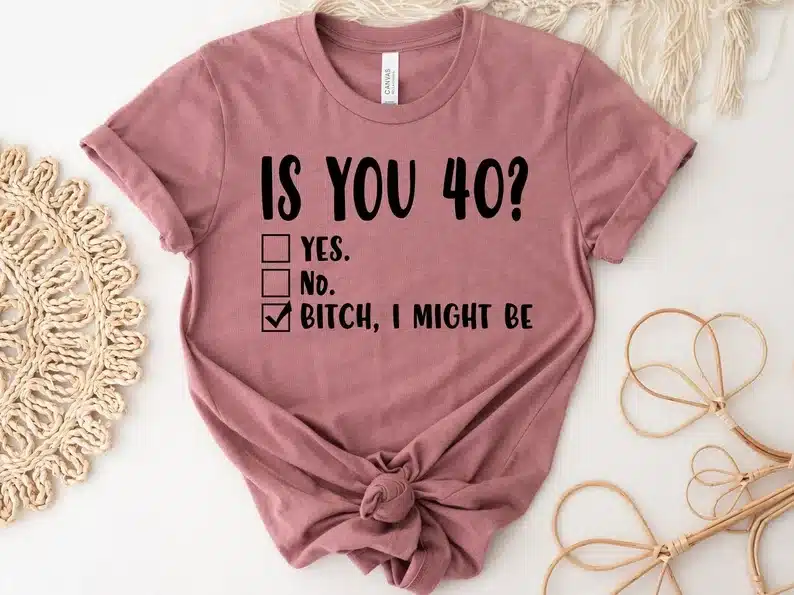 Dusty rose colored t shirt with black font that says Is you 40? and three boxes that say yes no and a check mark in the 3rd that says bitch, I might be. 