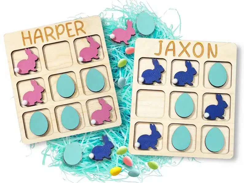 Wooden Easter Bunny tic tac toe, showing a pink bunny and blue egg set with the name HARPER on the top and a blue bunny and blue egg wooden set that says JAXON on top. 