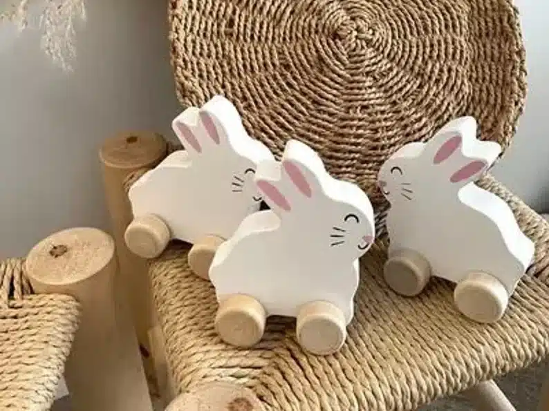 Three white wooden bunnies on wheels shown. 