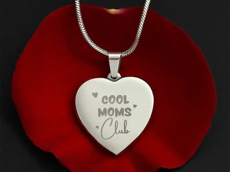 Silver chain with a large heart shaped charm that says COOL MOMS CLUB. 