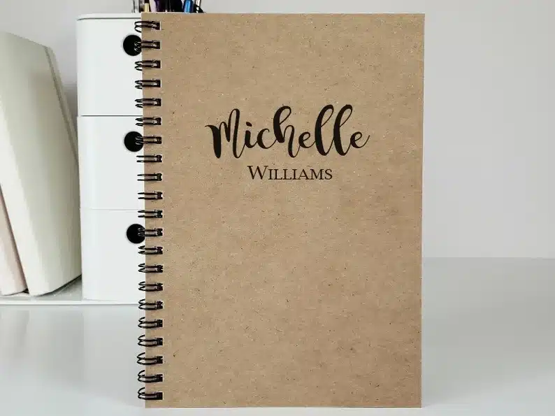 Brown personalized notebook that says Michelle Williams in black font. 