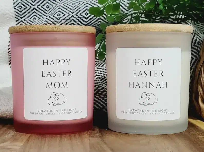 Two glass candles with wooden lids, both with personalized writing, one that's a pink candle says HAPPY EASTER MOM with a drawing of a bunny. the other a cream candle says HAPPY EASTER HANNAH with a drawing of a bunny. 
