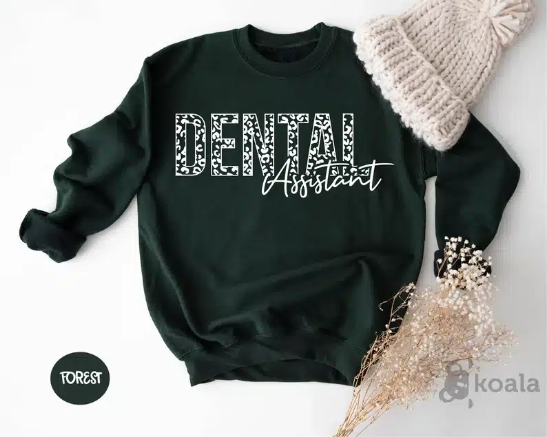 Above view of a black long sleeve sweatshirt with white font that says Dental assistant on it. 