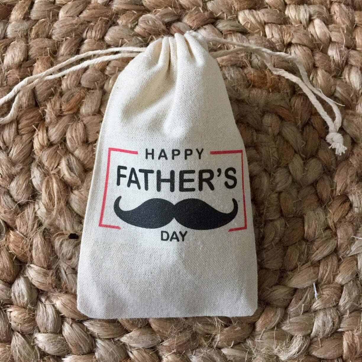 Tan drawstring bag that says Happy Fathers Day with a mustache on it in black. 